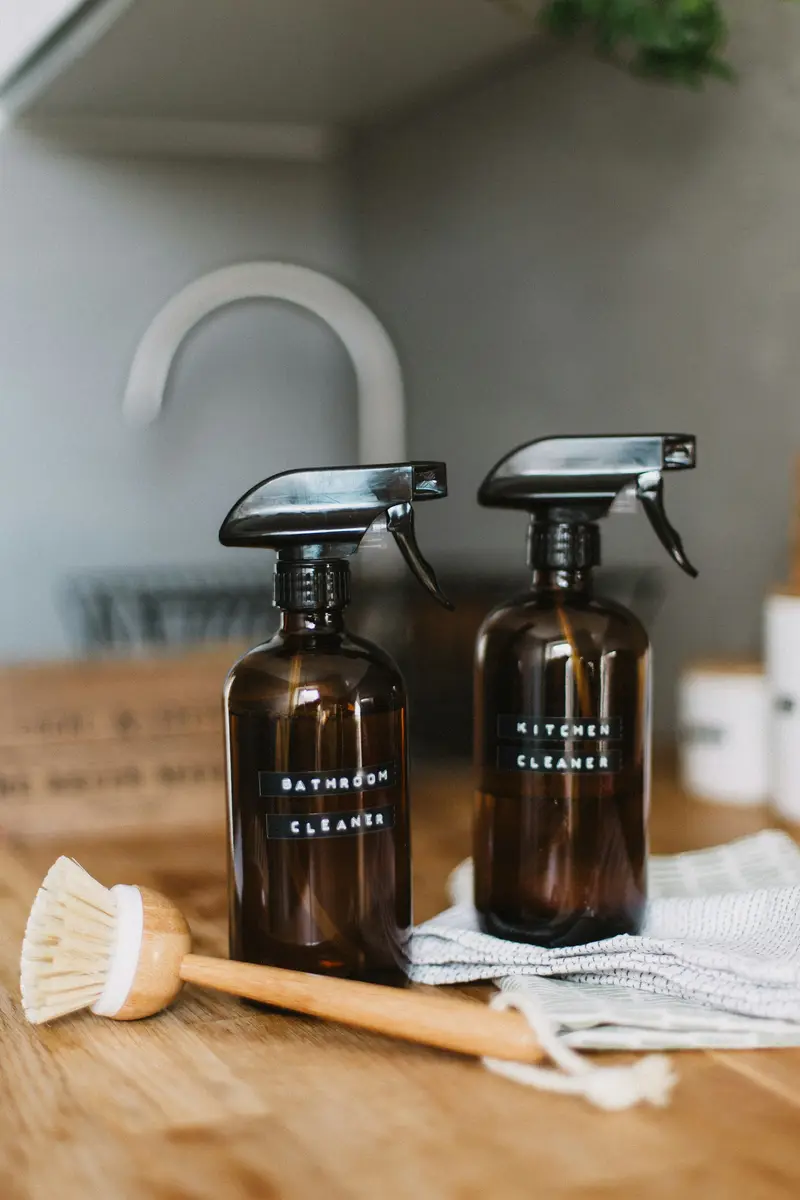 Eco-friendly glass spray bottles and brush on a worktop D&A Cleaning Ltd