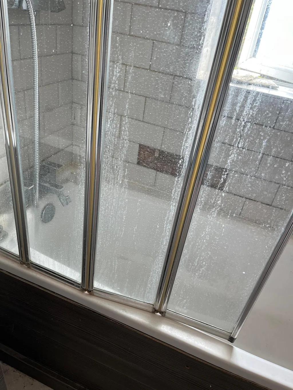 Folding bath shower screen clouded with limescale before cleaning